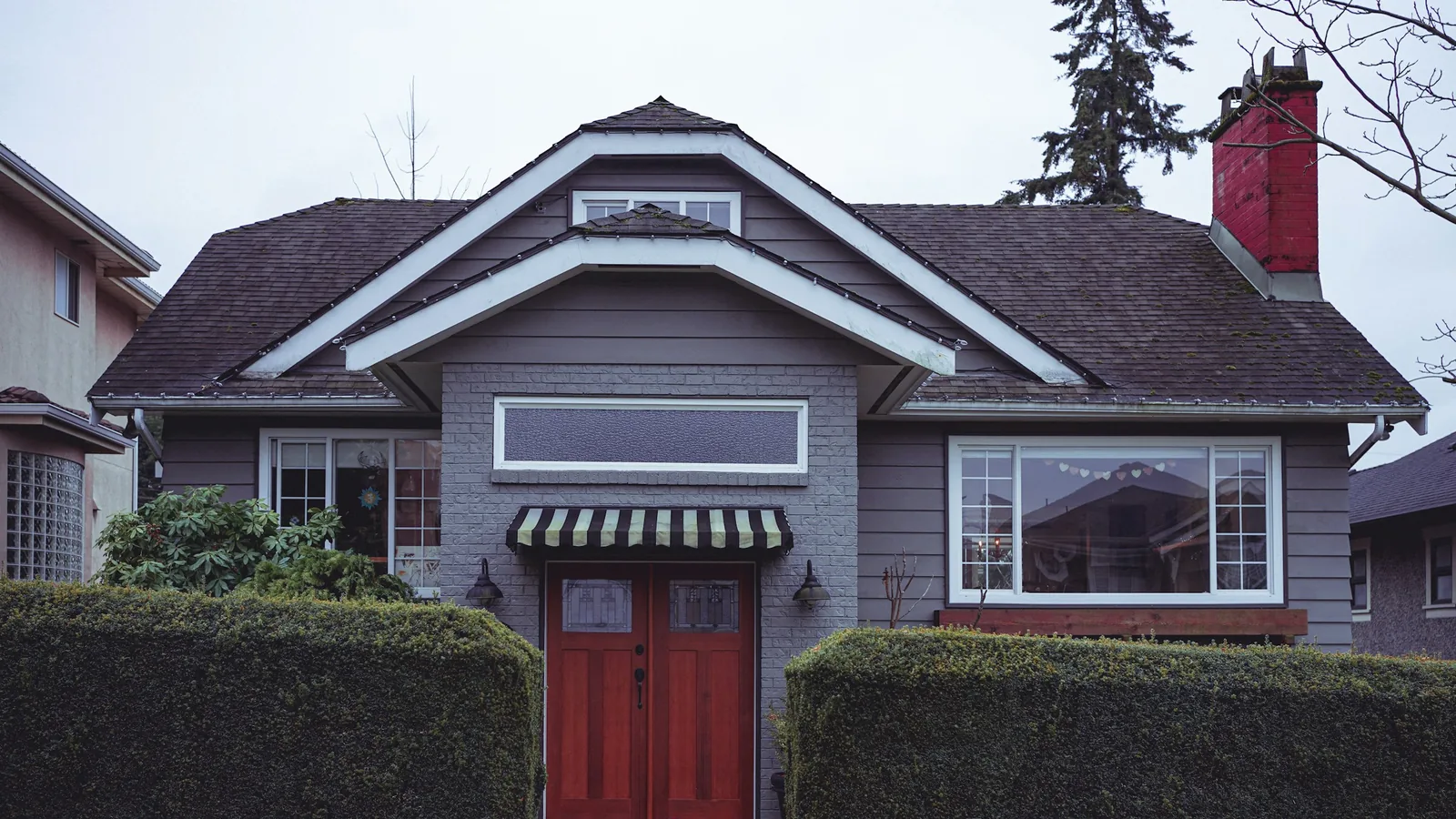 A gray house with a red door and a black and white awning, Vancouver