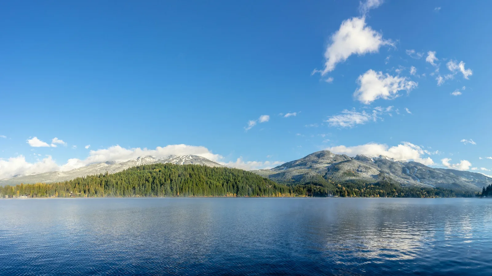 Calm BC lake with forested mountains and snow-capped peaks