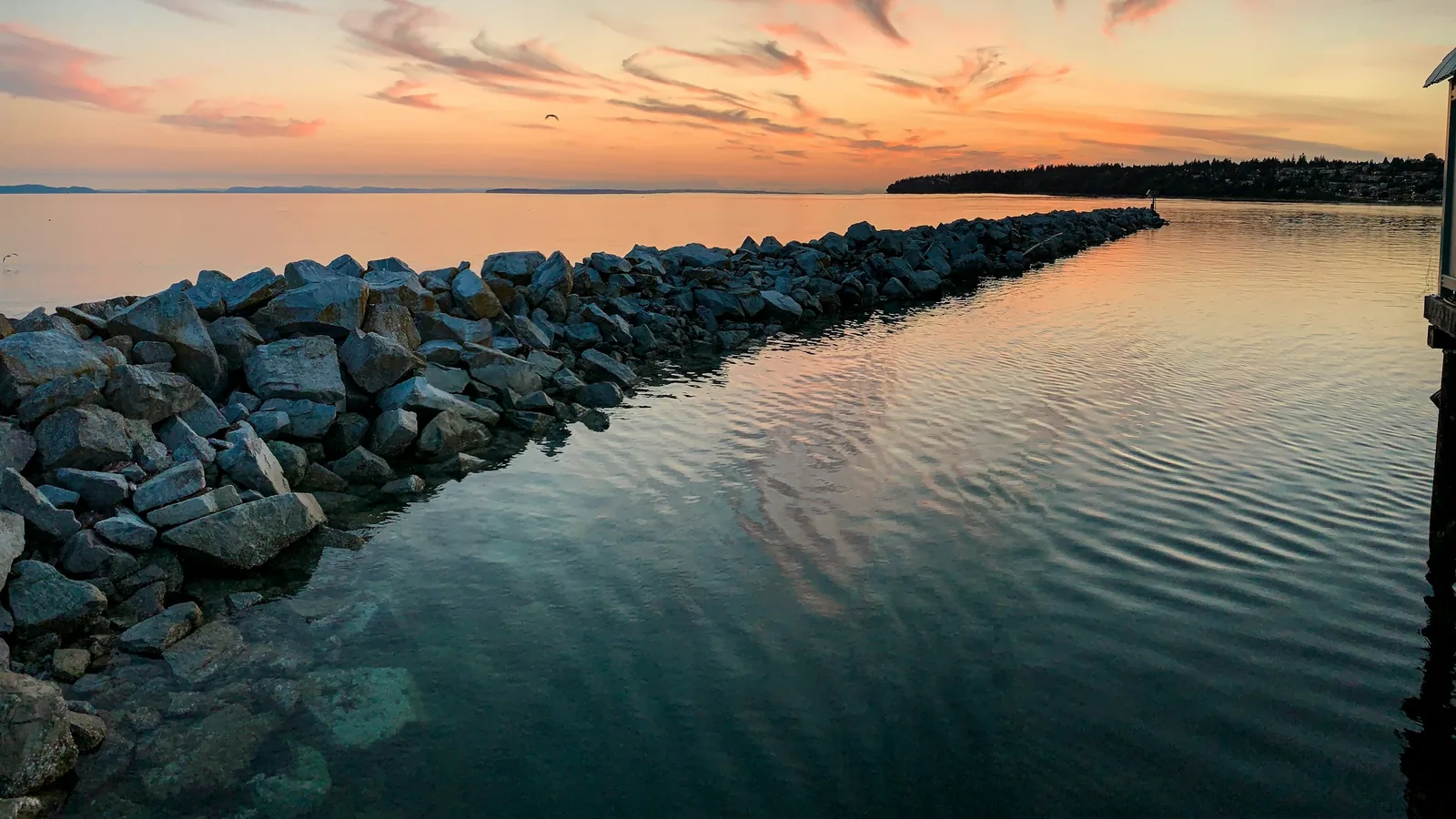 A dock with rocks in the water and a sunset in the background, the White Rock waterfront