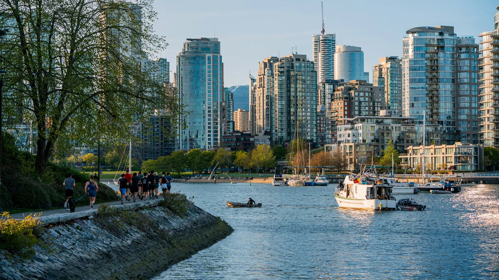 A group of people walking along a river next to tall buildings, Vancouver