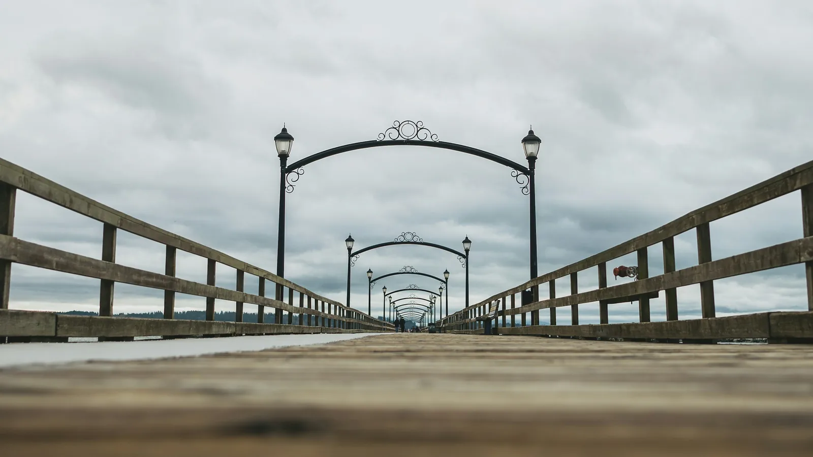 Wooden pier with arched lampposts under cloudy sky in the White Rock waterfront